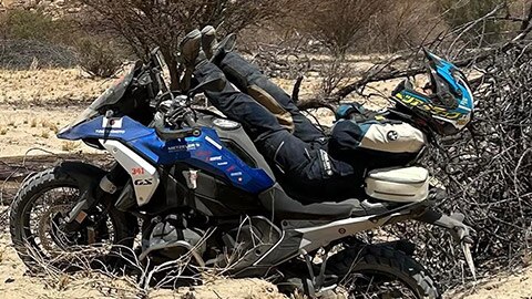 A rider on the Japanese women’s team lying on her R 1300 GS. Her legs are stretched out towards the handlebars, while her head and shoulders are protruding over the rear of the motorcycle.